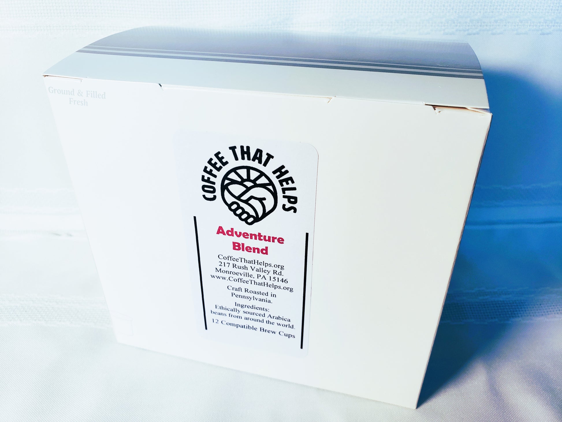 I brew cup box with the Coffee That Helps logo and the name "Adventure Blend" written on it.